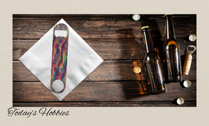 Colorful sublimation durable steel bottle opener on white napkin next to brown beer bottles and caps on wooden surface
