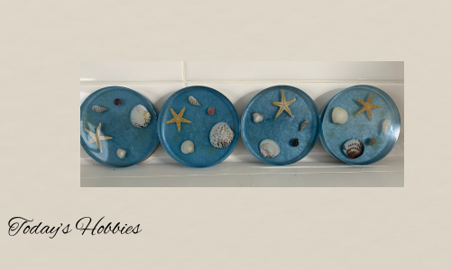 Set of four resin indoor outdoor decorative drink coasters with blue background and embedded seashells and starfish